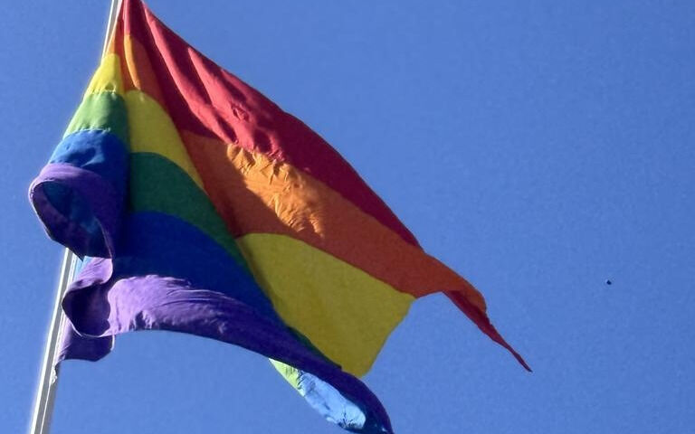 Prideflagget vaier i flaggstanga ved rådhuset i Fauske.
 Foto: Ida Bjørkquist, Fauske kommune